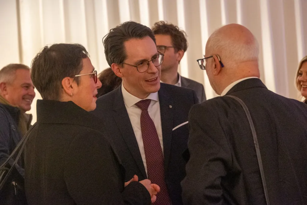Mehrere festlich gekleidete Gäste stehen bei einem Empfang im Gespräch beieinander.