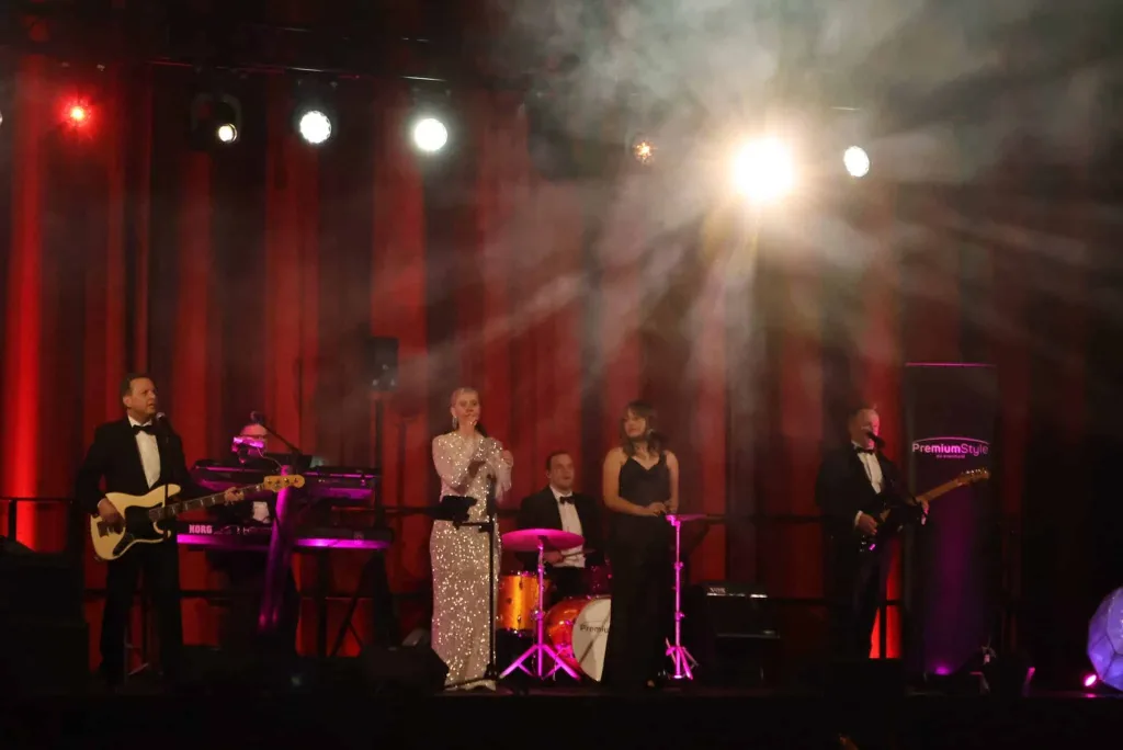 Band mit zwei Sängerinnen und Gitarrist auf einer beleuchteten Bühne