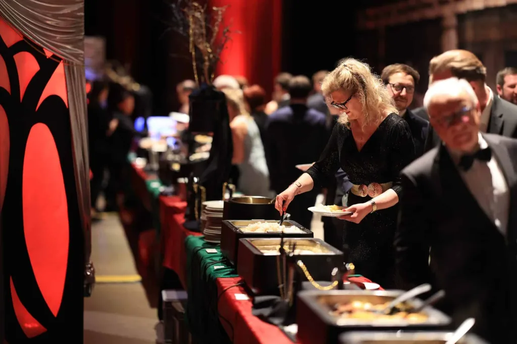Gäste bedienen sich an einem Buffet in einem festlich beleuchteten Innenraum.