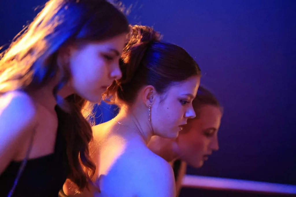 Drei Frauen stehen in einer Reihe und blicken im blauen und violetten Licht zur Seite.