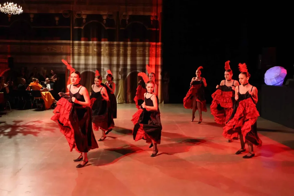 Mehrere Tänzerinnen in roten und schwarzen Flamenco-Kleidern bewegen sich auf einer beleuchteten Tanzfläche.