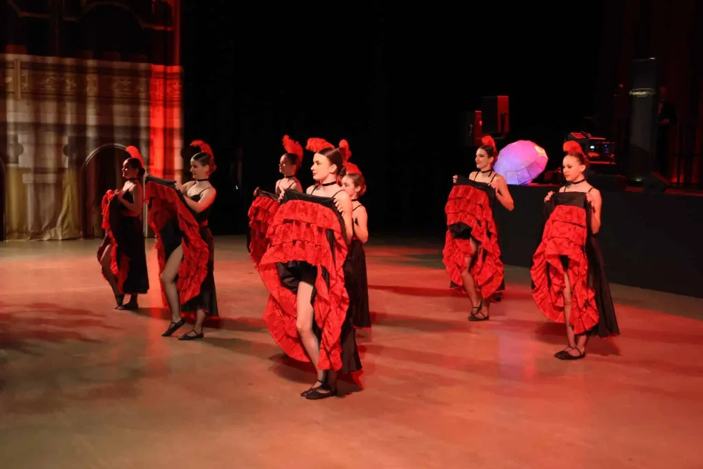 Mehrere Tänzerinnen in roten Flamenco-Kleidern stehen und tanzen auf einer beleuchteten Bühne.