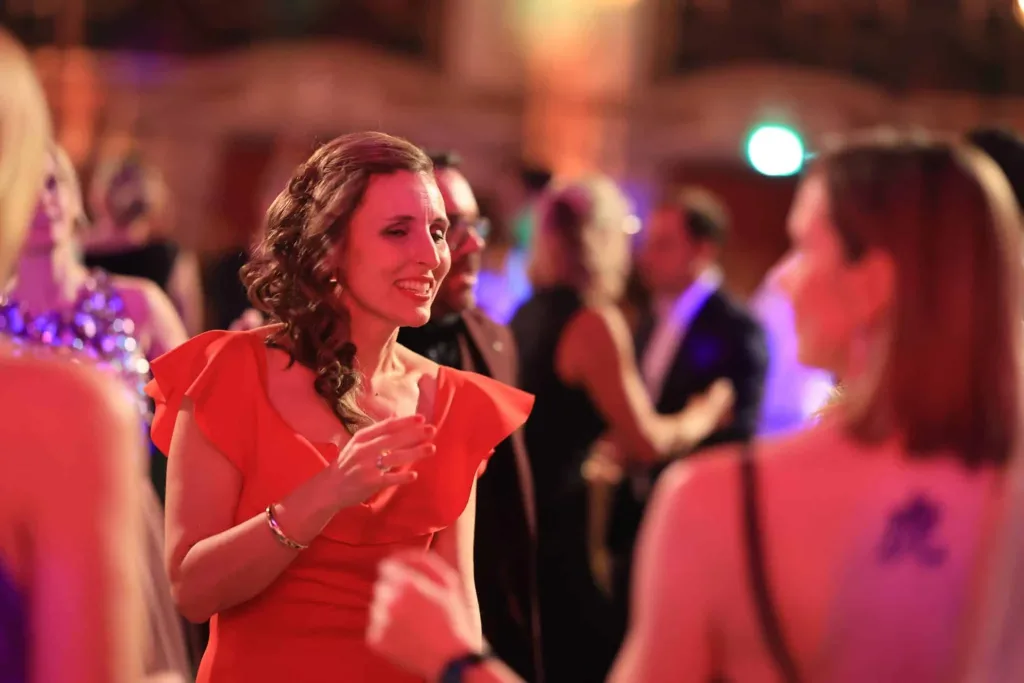 Frau in rotem Kleid spricht in festlicher, stimmungsvoll beleuchteter Ballatmosphäre mit anderen Gästen.
