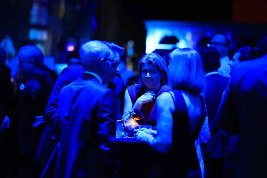 Mehrere elegant gekleidete Menschen unter blauem Licht im Gespräch an einem Tisch
