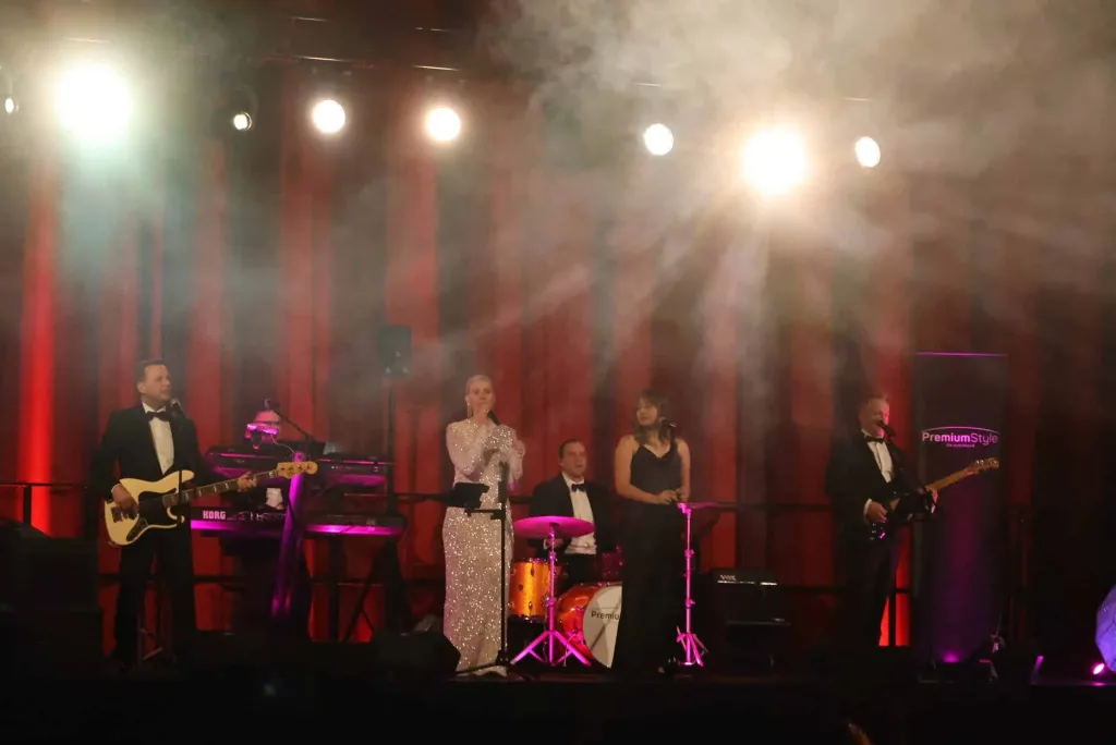 Fünf Musikerinnen und Musiker stehen mit Instrumenten auf einer beleuchteten, von rotem Licht und Bühnennebel erfüllten Bühne.