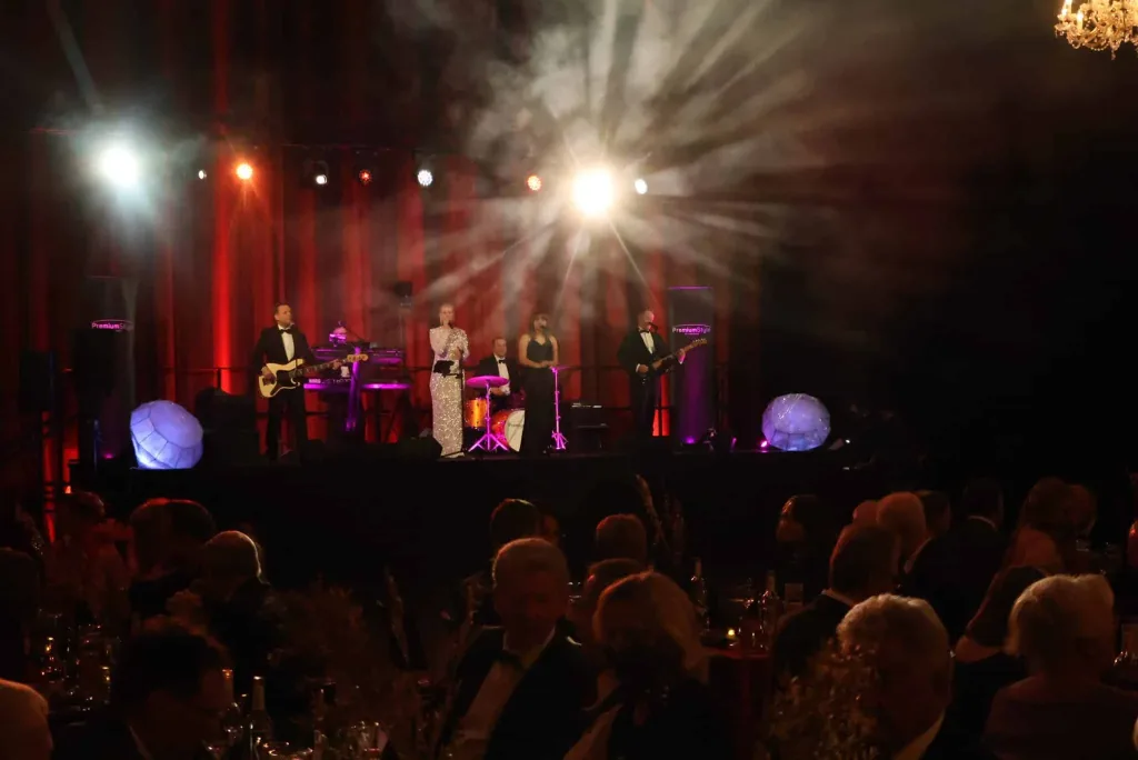 Liveband auf einer beleuchteten Bühne vor sitzendem Publikum