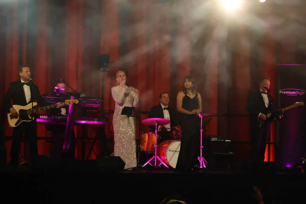 Liveband mit Sängerin auf einer beleuchteten Bühne vor roten Vorhängen