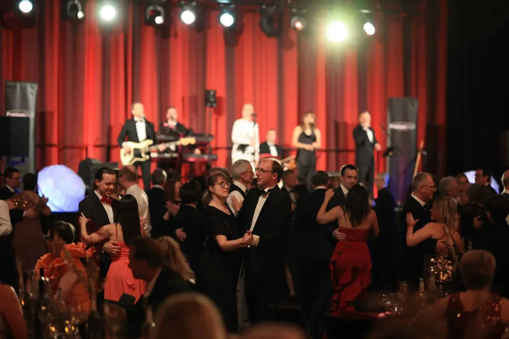 Tanzende Gäste vor einer Bühne mit Liveband und roter Beleuchtung