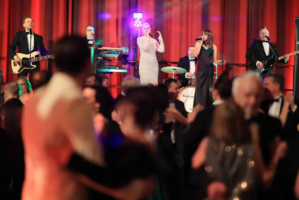 Liveband mit Sängerinnen und Musikern auf einer beleuchteten Bühne, davor tanzendes Publikum