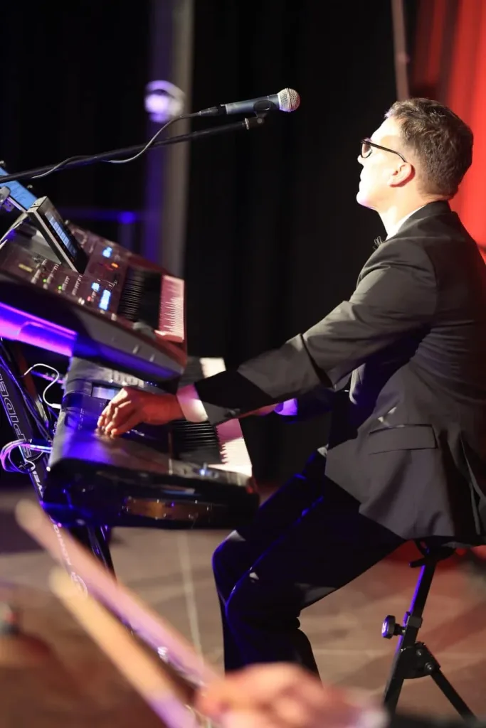 Musiker im schwarzen Anzug spielt an einem Keyboard und singt in ein Mikrofon.