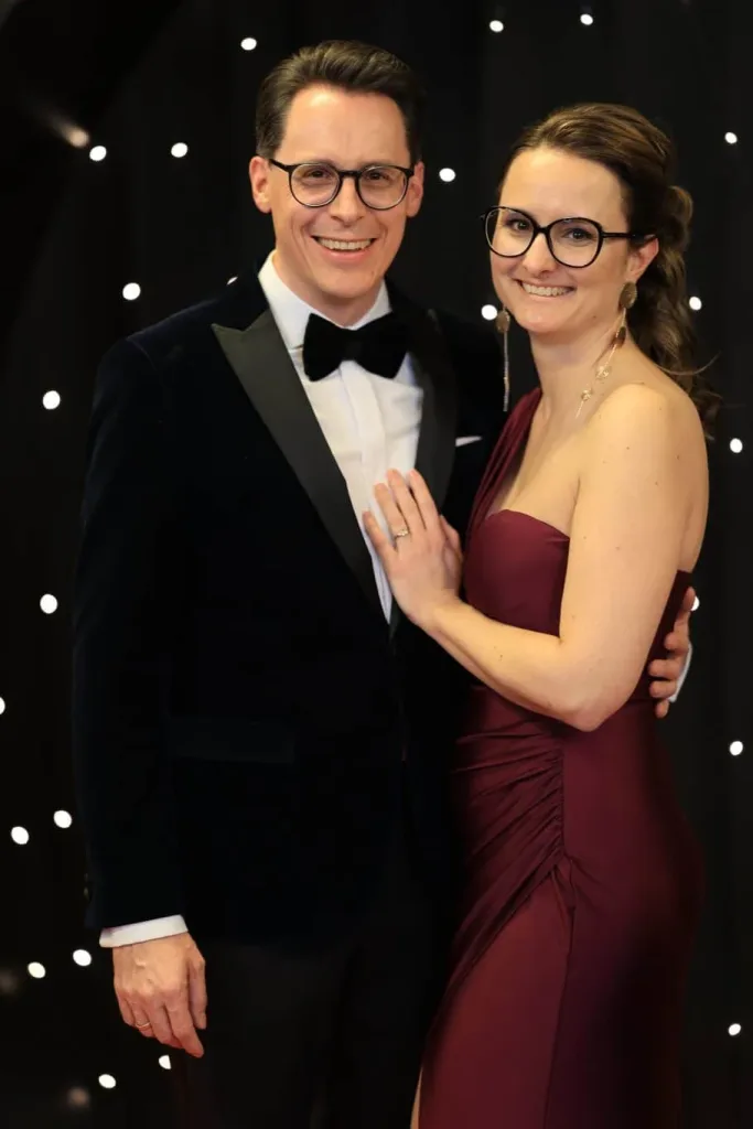 Paar in schwarzem Smoking und bordeauxrotem Abendkleid vor einem schwarzen Hintergrund mit Lichtpunkten