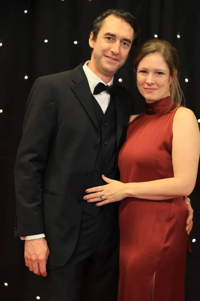 Paar in schwarzem Anzug und rotem Abendkleid vor einem dunklen Hintergrund mit Lichtpunkten