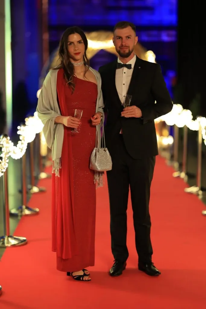Eine Frau im roten Abendkleid und ein Mann im schwarzen Smoking stehen auf einem roten Teppich.