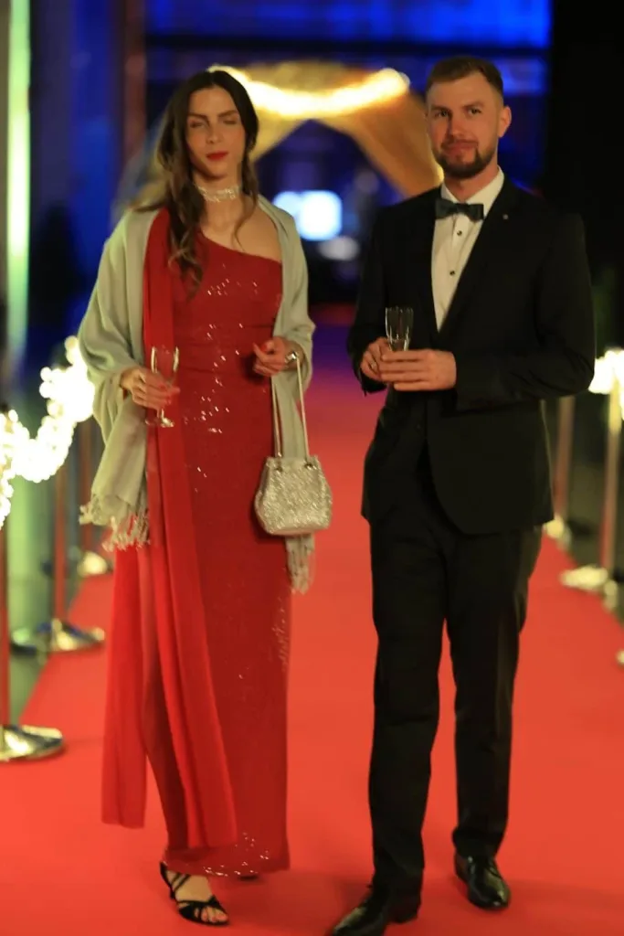 Elegantes Paar auf einem roten Teppich; die Frau trägt ein rotes Kleid, der Mann einen schwarzen Smoking.