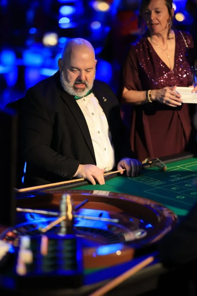 Ein Mann bedient an einem Roulettekessel den Spieltisch, während eine Frau daneben steht.
