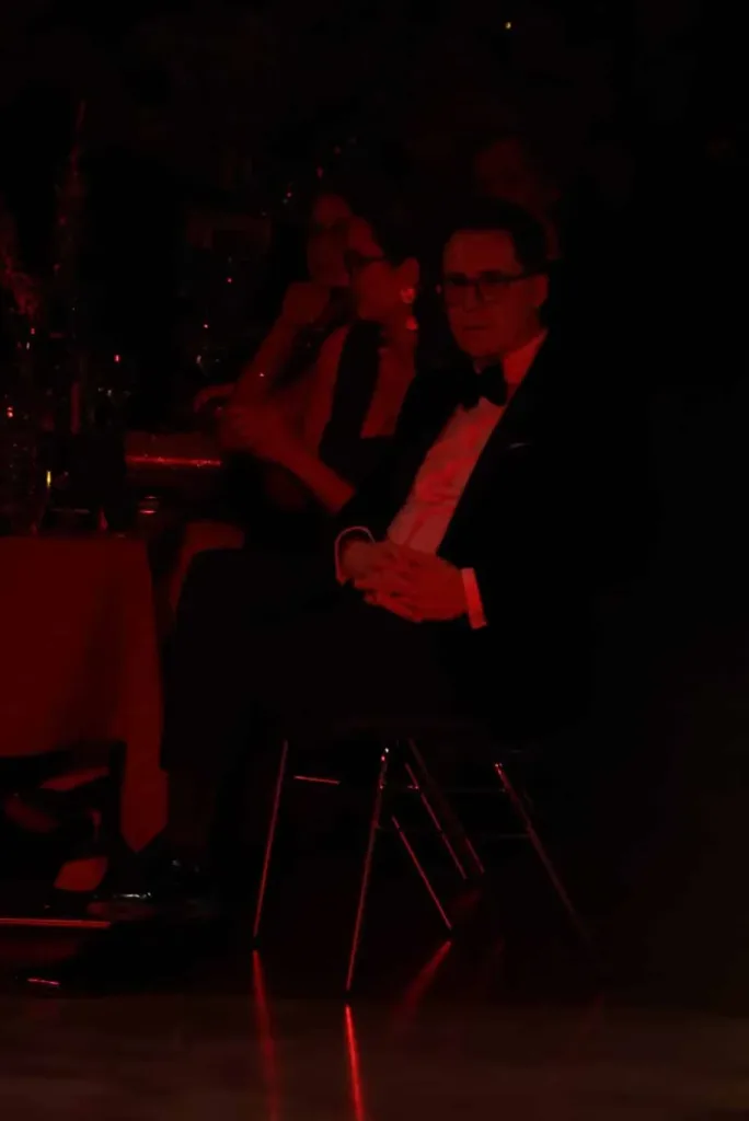 Ein elegant gekleidetes Paar sitzt in einem abgedunkelten Raum mit roter Beleuchtung.
