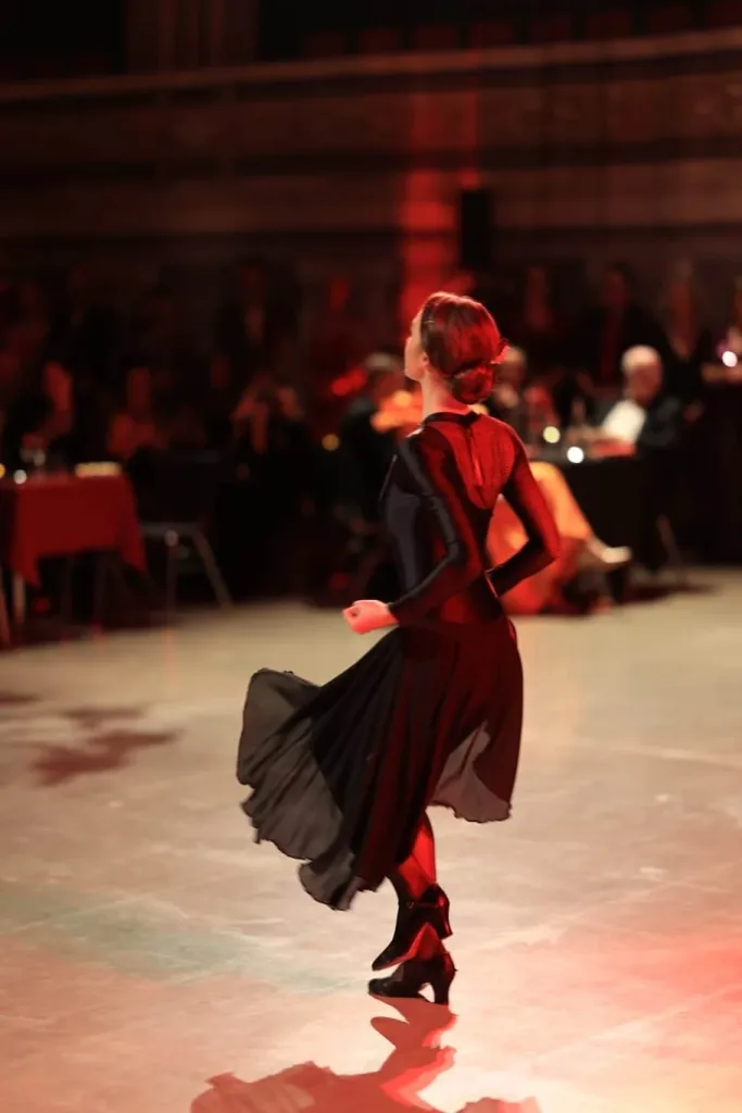 Eine Frau in einem roten Kleid tanzt mit ausgebreitetem Rock über eine beleuchtete Tanzfläche.