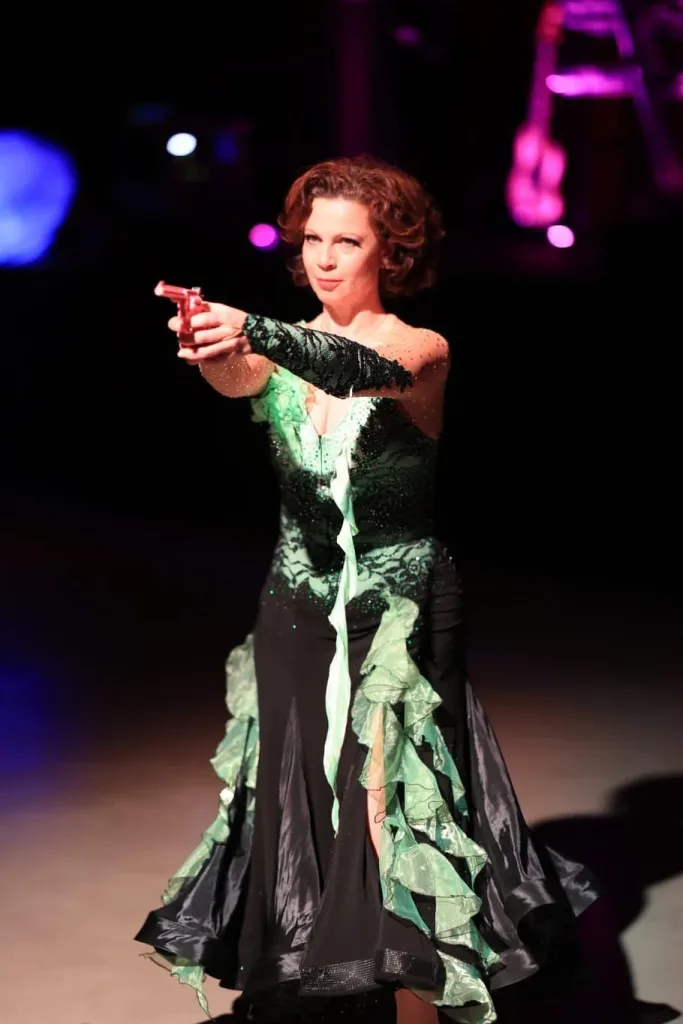 Tänzerin in einem schwarzen und grünen Abendkleid zeigt mit ausgestrecktem Arm ins Publikum.