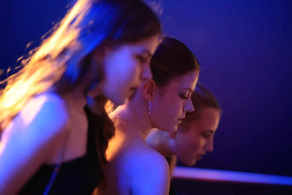 Drei Frauen tanzen in einer Reihe in blau-violetter Beleuchtung.