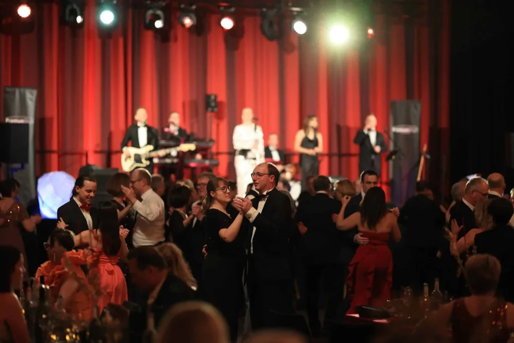 Tanzende Paare in einem festlich beleuchteten Saal vor einer Bühne mit Liveband