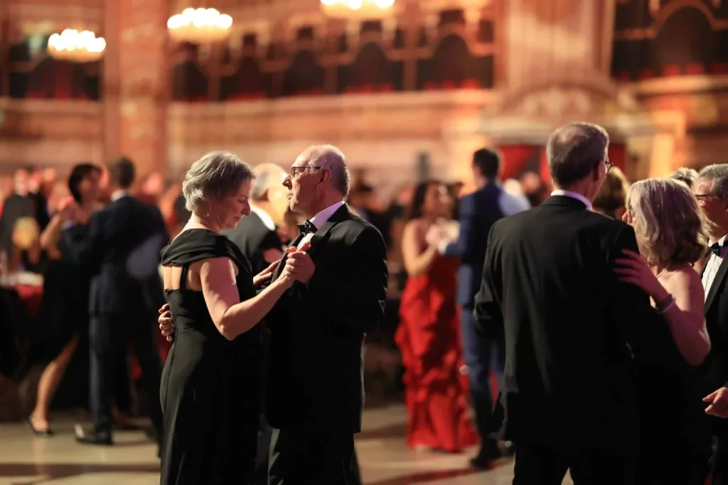 Mehrere elegant gekleidete Paare tanzen in einem festlich beleuchteten Saal.