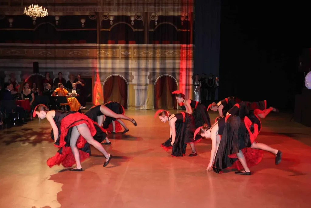 Tanzgruppe in roten und schwarzen Kostümen bei einer Choreografie auf einer festlich beleuchteten Bühne