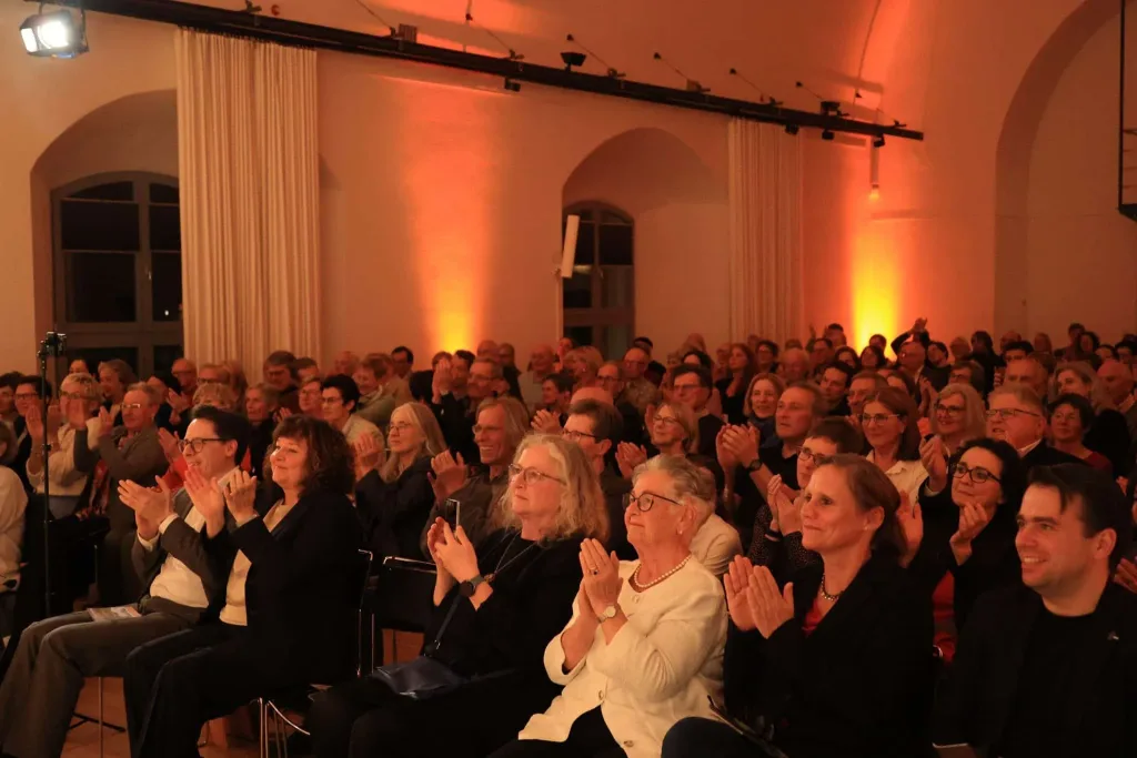 Publikum applaudiert in einem warm beleuchteten Konzertsaal.