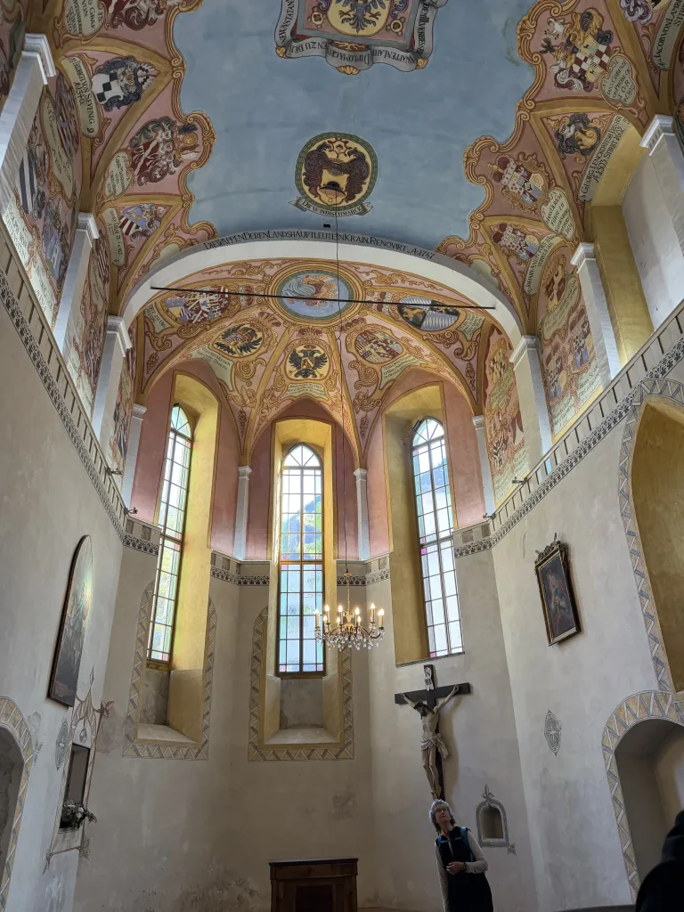 Blick in den reich mit Fresken ausgemalten Altarraum einer Kirche mit hohen Fenstern, Kronleuchter und Kruzifix
